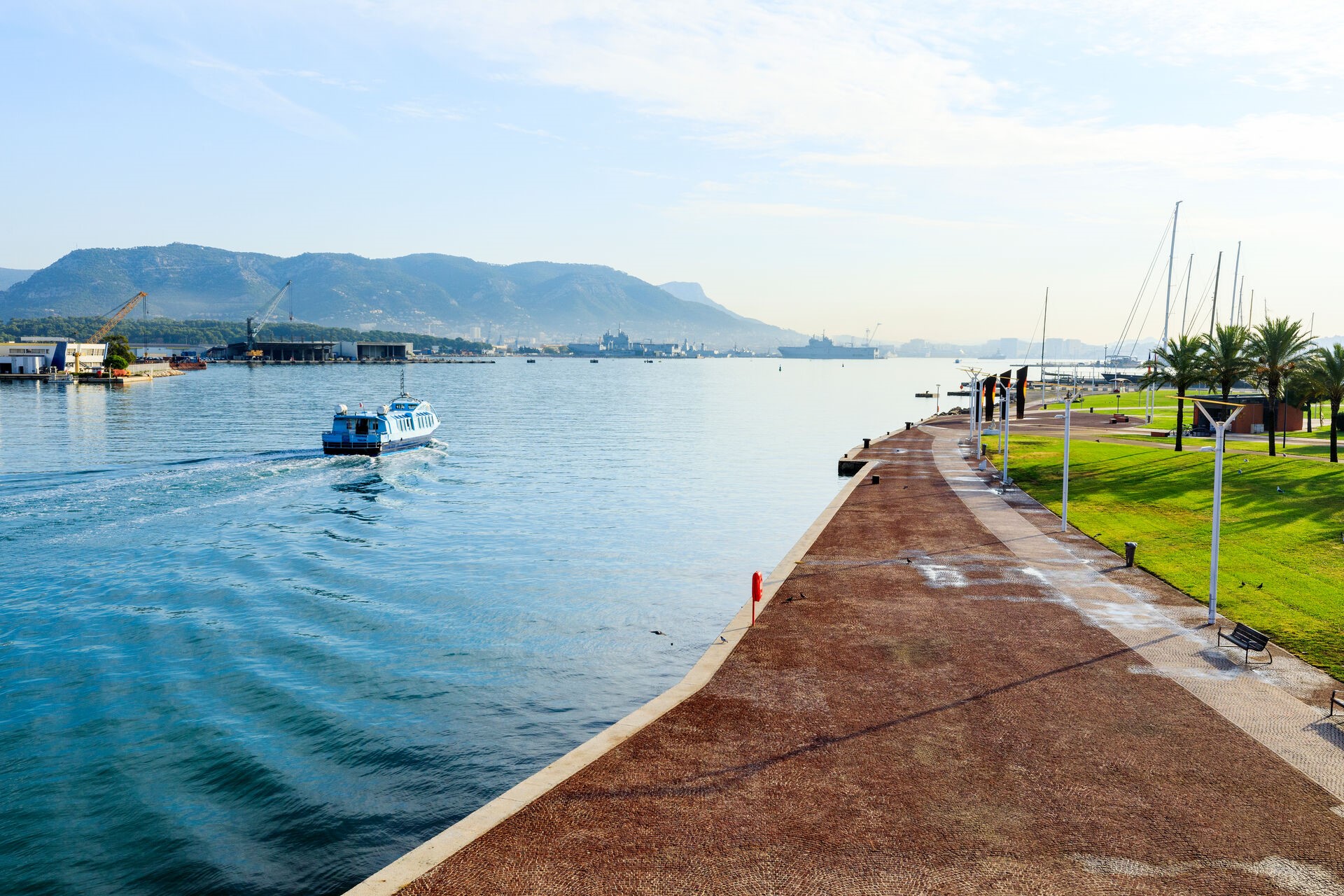 Vue sur une navette maritime depuis le quai au départ du Port de la Seyne, avec les bateaux militaires de l'Arsenal de Toulon en arrière-plan