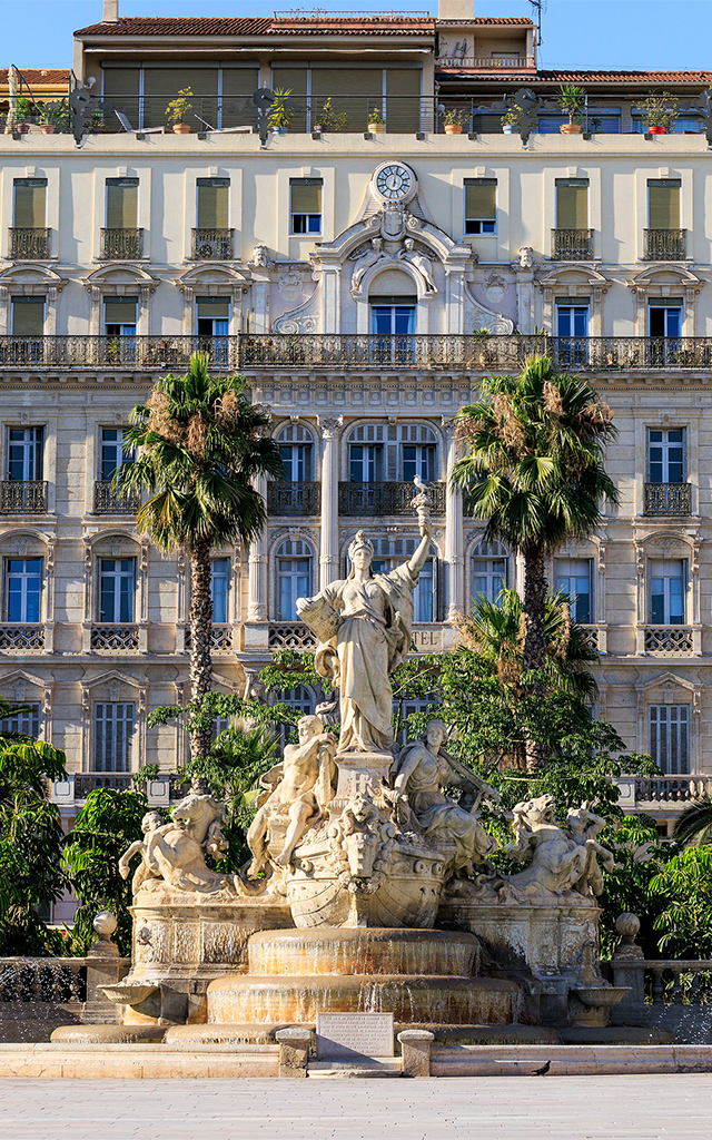 Fontaine de la Place de la Liberté au premier plan, bâtiments de style Haussmannien à l'arrière-plan